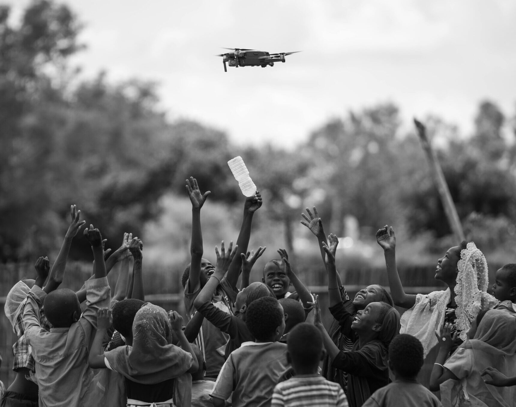 A group of African children joyfully reaching towards a flying drone.